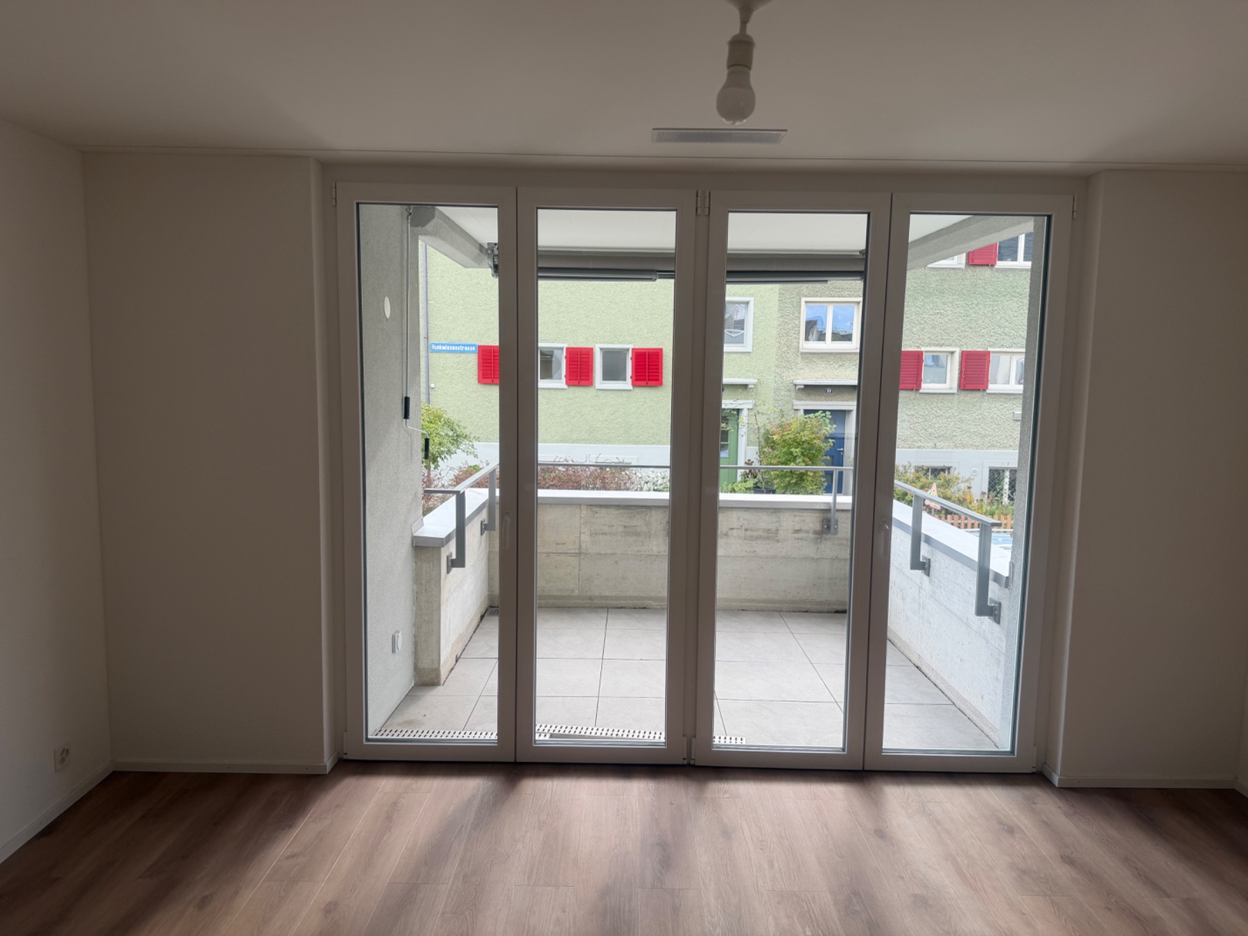 Balkontüre mit zwei Flügeln und Sicht auf den Balkon. Der Raum zeigt Parkett/Laminat und einen aufgeräumten Zustand.