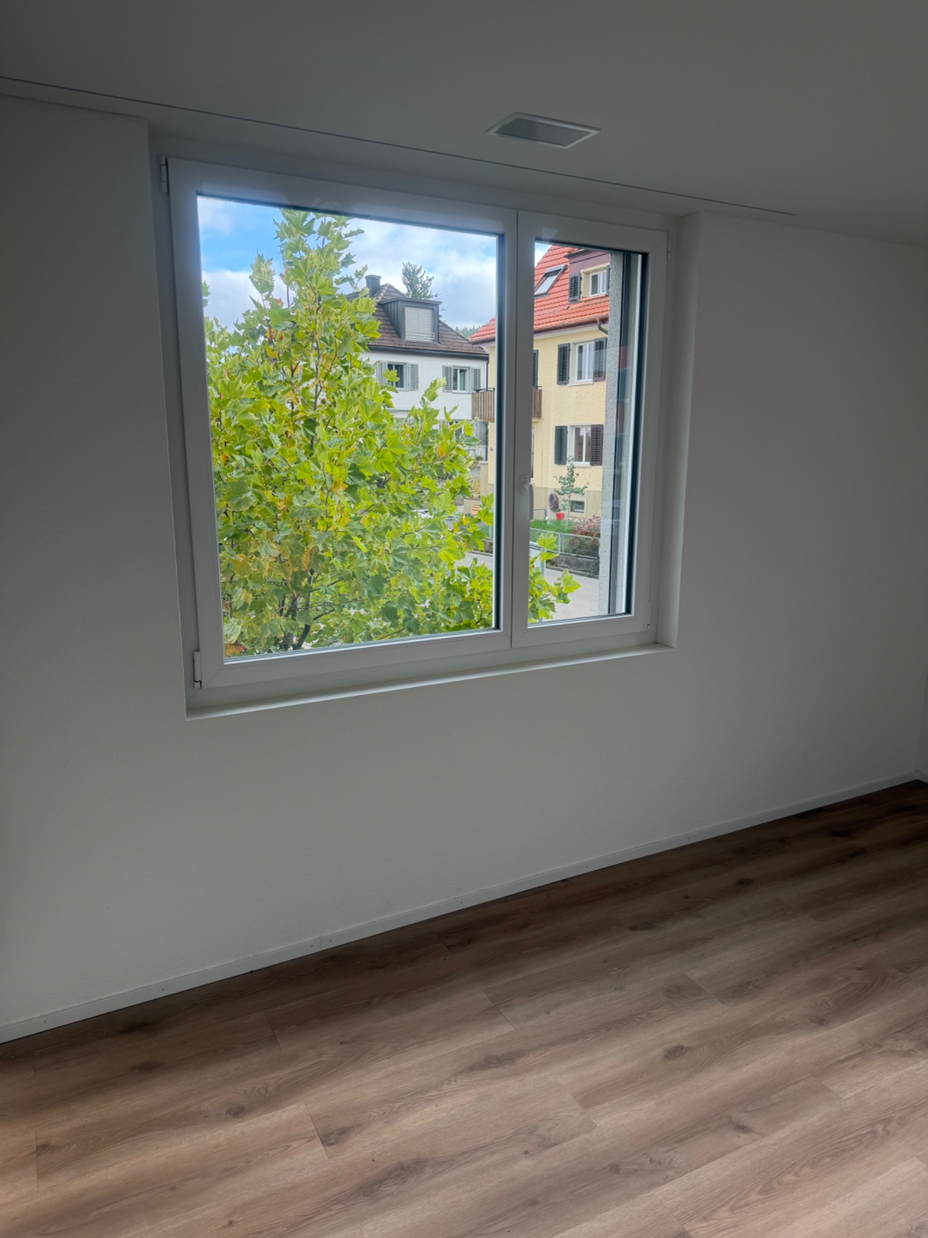 Leerer Raum mit Fensterfront und Blick ins Grüne. Boden und Wandflächen wirken sauber und ungestört.