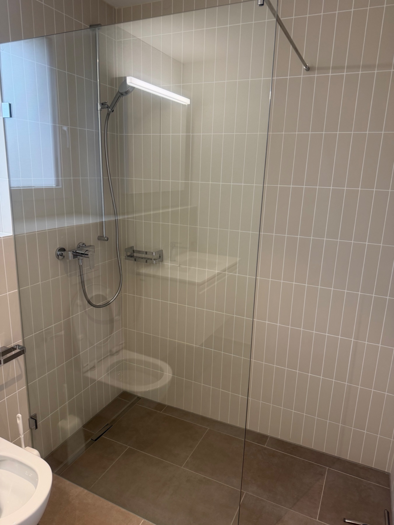 Dusche mit Echtglas und Duschkopf/Armaturen. Boden und Wandflächen wirken gereinigt, ohne sichtbaren Schmutz.